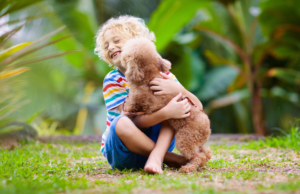 A little child embracing a puppy in the grass while parents wonder how to stop the puppy jumping behavior.